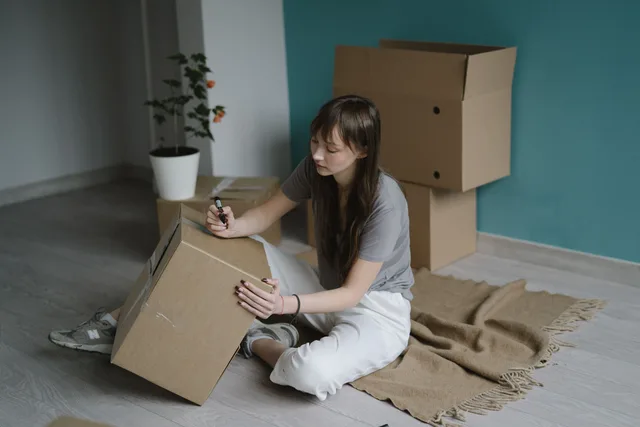Young woman labeling a cardboard box while sitting on the floor. Moving or packing concept. Why the last rooms in an organized makeover always suffer most