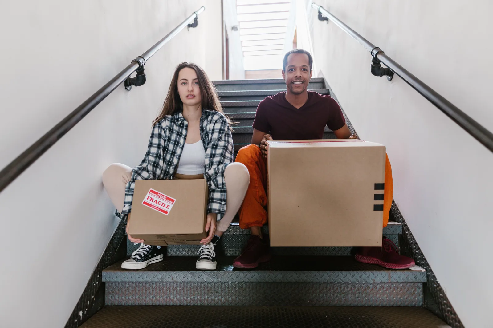 Interracial couple sitting on stairs with cardboard boxes, ready for moving. Hiring help for small-space storage: the questions worth asking first