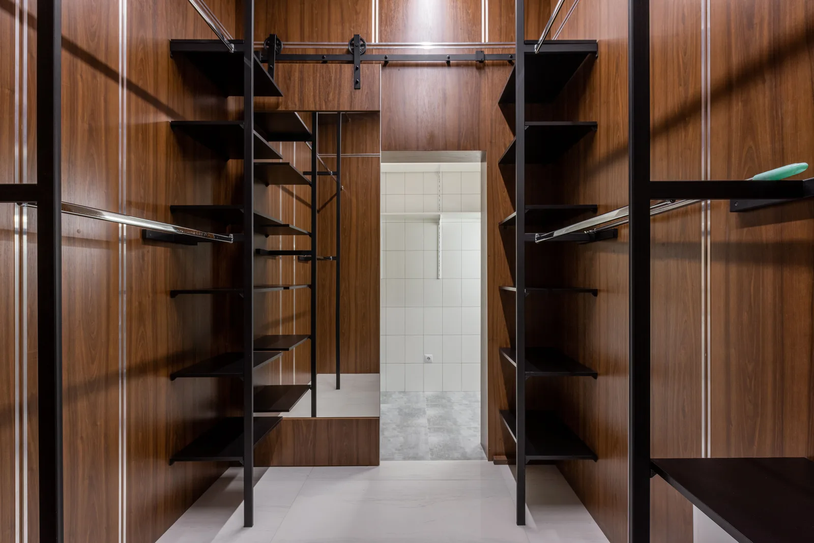 Empty black shelves and racks placed in modern walk in closet with brown walls and mirror with reflection at home. Particleboard, plywood, steel, or wire: storage systems materials compared