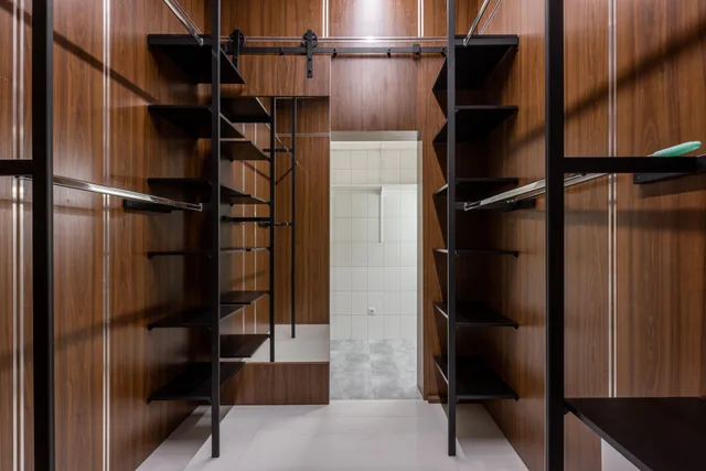 Empty black shelves and racks placed in modern walk in closet with brown walls and mirror with reflection at home. Particleboard, plywood, steel, or wire: storage systems materials compared