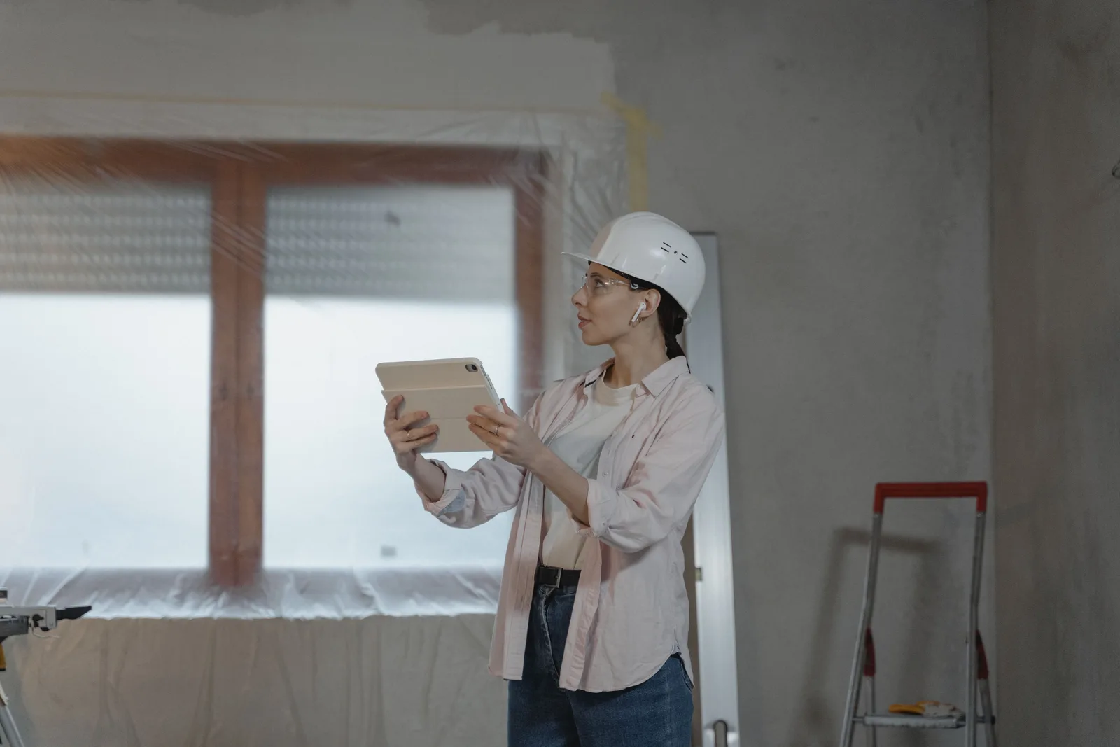 A female architect wearing a hard hat uses a tablet on a construction site for interior design planning. Organization mistakes: the questions to ask before hiring anyone to fix them